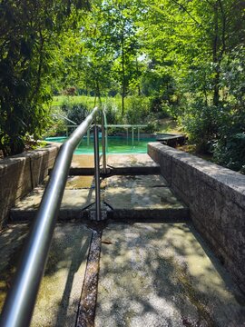 Wassertretbecken im sonnendurchfluteten Kurpark in Brilon (Sauerland). Edelstahlgel&auml;nder und Steinstufen f&uuml;r gesundheitsf&ouml;rderndes Wassertreten, Entspannung und Erfrischung in der Natur.
