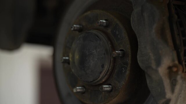 A mechanic using a hammer to hit a rusty car wheel hub assembly near the brake rotor and caliper.