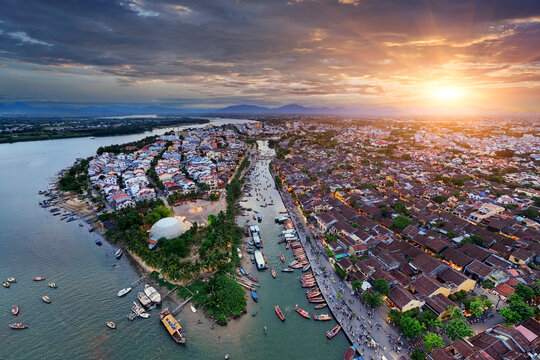 Boats float on the Thu Bon River in Hoi An Vietnam during bright sunset. The sky shows colors as the day ends