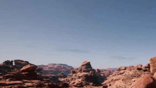 Scenic view of large rock formations in a desert area. The sun shines bright and highlights the natural beauty. The horizon shows distant hills and a clear blue sky.