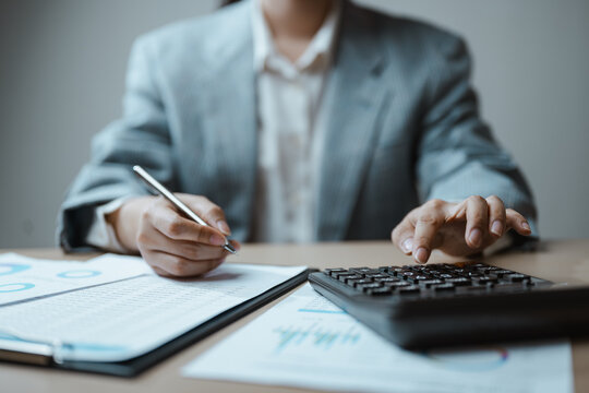 An accountant records figures during financial bookkeeping, using a calculator, paperwork and a business report to organize accounting, tax, receipt and tracking data for reliable financial control.