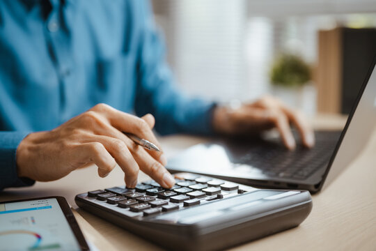 An accountant uses a calculator to review finance figures for budgeting and accounting, comparing expense, revenue, profit and cost in a financial report that informs finance planning and strategy.