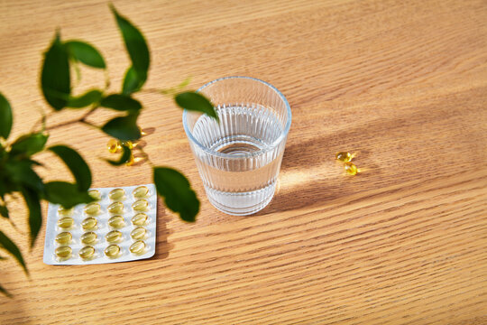 Glass of Water with Vitamin Supplement Capsules on Wooden Table