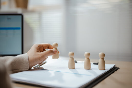A hiring manager selects one employee figure from a group as recruitment and management evaluate employees, resources and job needs while staff search and human assessment shape hiring decisions.