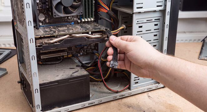 Close up view of technician hand plugging internal power cable connector into motherboard inside opened personal computer tower case
