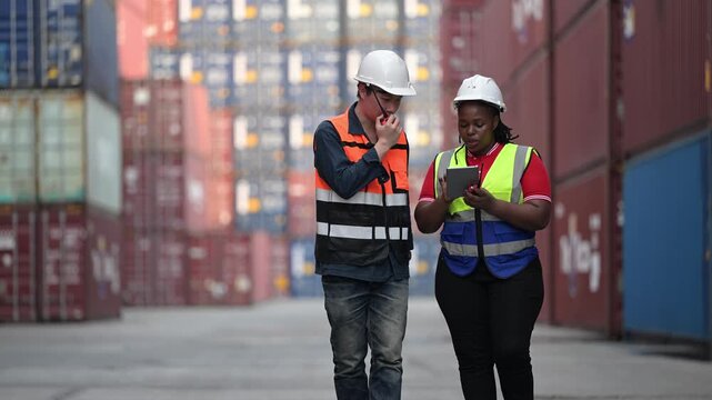 Logistics workers review operational data while inspecting shipping containers at a cargo yard. Concept of supply chain, freight transport, warehouse operations, teamwork, and logistics management.