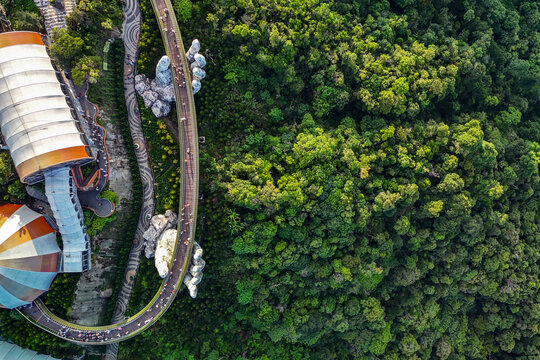 Visitors walk along the Golden Bridge supported by giant stone statues situated in the middle of a lush green forest at Ba Na Hills in Vietnam
