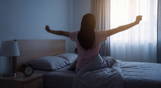 Back view of woman stretching both arms after waking up in comfortable bed during early morning at home