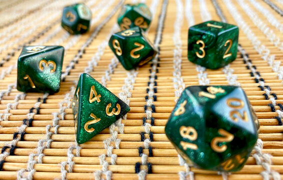 Emerald green glitter rpg polyhedral dice set with gold numbers on bamboo mat background for MTG life counter tabletop gaming blogs or fantasy card game accessory shop advertising.