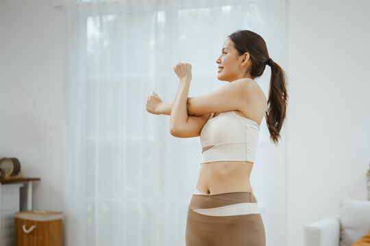 A woman performs an upper-body stretch at home, bringing fitness, exercise, wellness and active movement into a lifestyle that builds flexibility, energy and confidence through lifestyle habits.