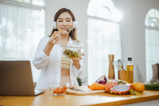 A woman tastes a fresh salad of vegetables and fruit in her kitchen, showing healthy cooking with natural ingredients, clean food and balanced nutrition for a meal that sustains a healthy diet.