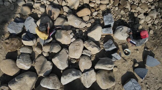 Aerial view of workers using hammers to break large river stones in a quarry in Karanglewas, Central Java, Indonesia.
