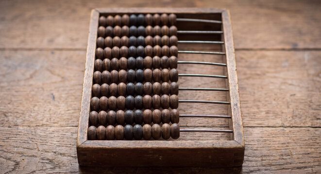 An antique wooden abacus with sliding beads sits on a weathered wooden surface representing ancient arithmetic mathematics and calculating tools