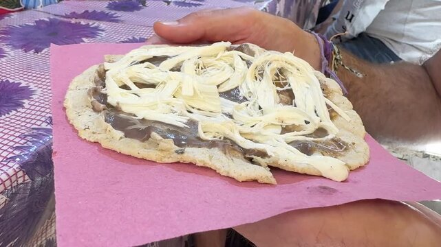 Hand Holding Traditional Oaxacan Memela Corn Cake with Beans and Quesillo Cheese