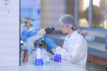 A pair of female lab technicians in white coats, protective eyewear and sterile hairnets focusing...