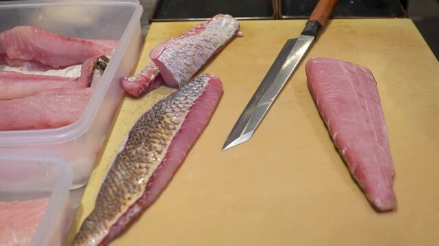 Chef preparing fresh fish fillets on a cutting board, showing seafood processing, knife skills, raw fish preparation, and professional kitchen work.