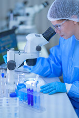 A female medical researcher in a white lab coat, hairnet and clear safety goggles resting a gloved...
