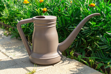 Watering can standing beside a flower garden on a sunny summer day. Gardening tool surrounded by green plants and marigold flowers, plant care and outdoor gardening concept. © marinasokolchik