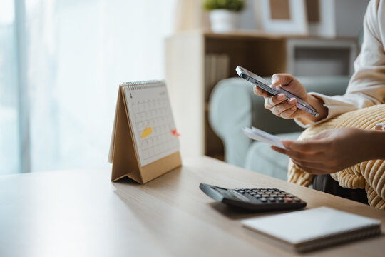 A person checks a smartphone beside a calculator, using a personal expense tracker for financial planning and budget decisions that organize money, payment and income within a personal report.