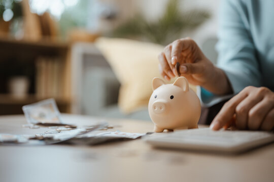 A person drops a coin into a piggybank and uses the piggybank to organize saving and money, aligning finance with deposit, budget and fund goals for retirement plus personal growth and future income.