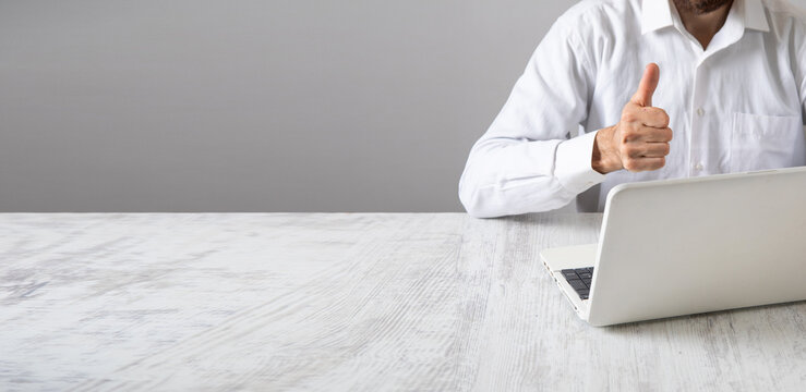 Caucasian businessman making thumb up gesture with a laptop computer.