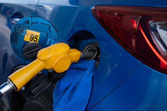 Yellow fuel nozzle inserted into a blue car marked for 95 octane gasoline at a station. Vehicle refueling, petrol consumption. Automotive energy use, travel cost and routine vehicle maintenance.