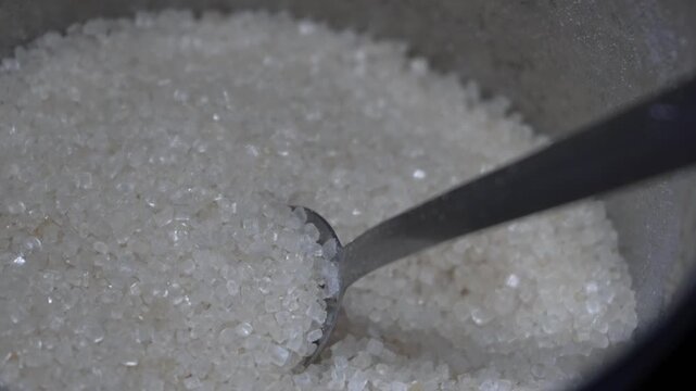Close-up of white granulated sugar crystals in a bowl with a spoon