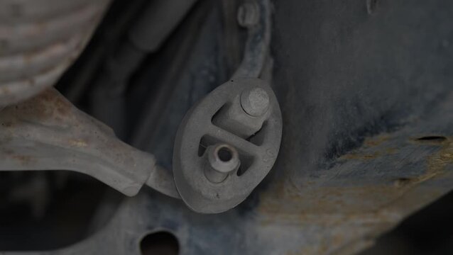 A rubber exhaust hanger insulator connecting a metal exhaust pipe rod to the car chassis mounting bracket.