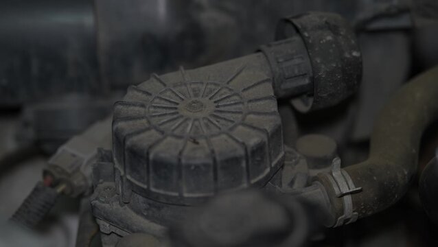A close-up view of a dusty black plastic PCV valve or oil separator cap located on a car engine.