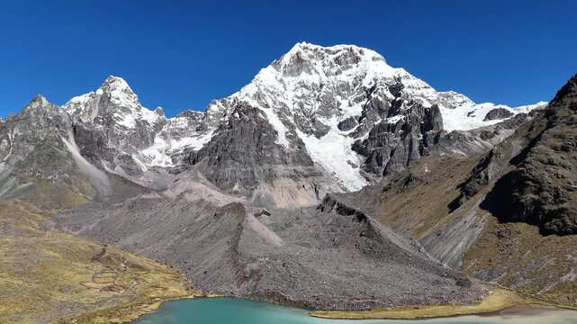 Cinematic aerial view sweeping across a high altitude glacial valley towards a towering snow mountain in Peru.