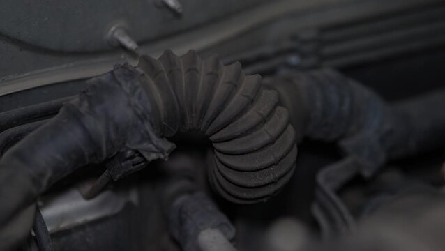 A dusty corrugated rubber boot protecting a wiring harness or cable conduit bent inside a car engine bay.