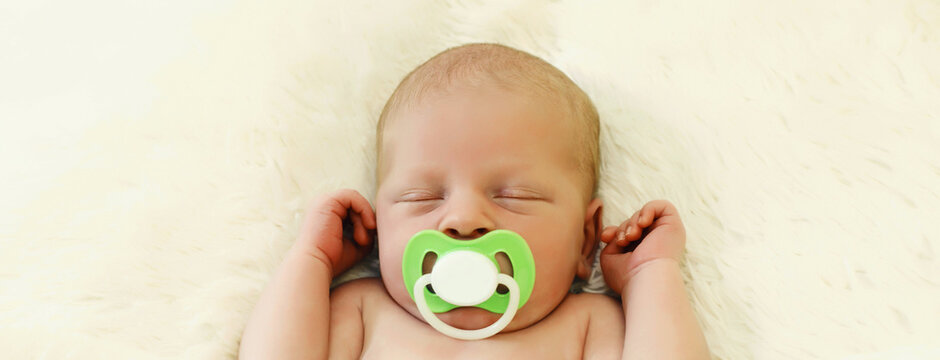 Portrait of sweet baby with pacifier, infant sleeping lying on white bed at home