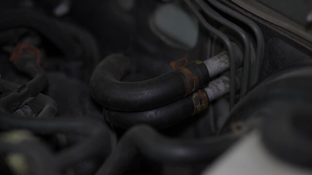Two black rubber heater hoses connected to metal firewall pipes with rusty spring clamps inside a car engine bay.