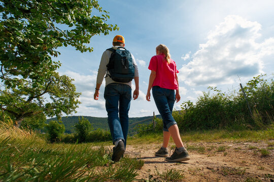 Two adults, a woman and a man, hiking on a sunny path in the countryside. Low angle shot with the blue sky.