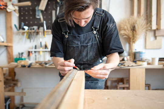 Focused skilled carpenter restorer working with vintage window frame at workplace in repair shop, concentrated master measuring size of wooden board for future replacement patch using ruler and pencil