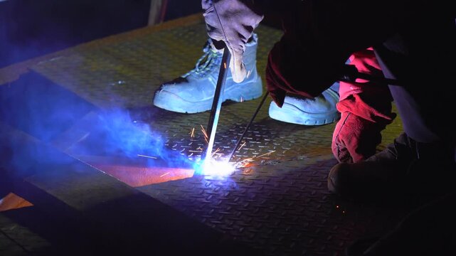 Welder Performing Stick Arc Welding on Metal Floor Surface Close Up With Bright Sparks in Industrial Environment