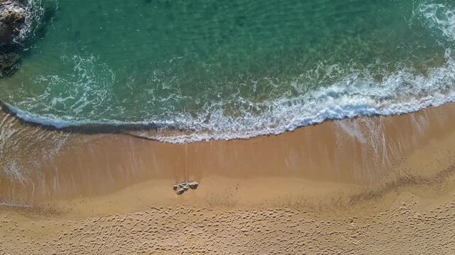 Aerial view of turquoise waves washing over the sandy beach in Lloret de Mar, Catalonia, Spain.