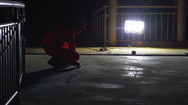 Construction Worker Grinding Surface with Angle Grinder at Night Under Bright Spotlight