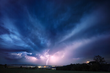 Obraz premium Lightning bolt and clouds in dramatic dark blue night sky. A real natural weather photo of a thunderstorm. 