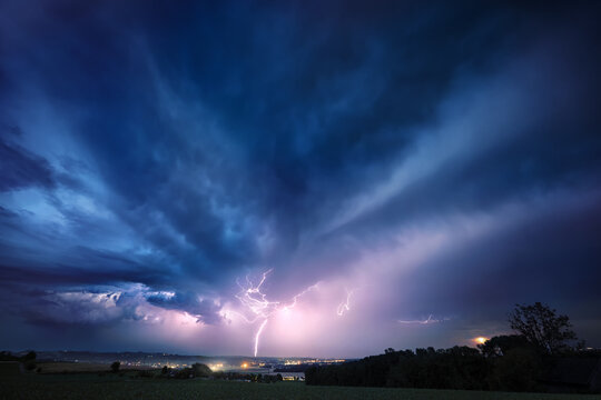Lightning bolt and clouds in dramatic dark blue night sky. A real natural weather photo of a thunderstorm. 