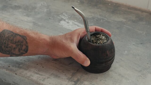 Male hand with a tattoo holding a traditional calabash gourd for drinking yerba mate tea