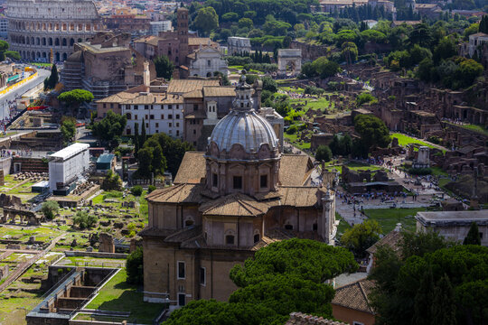 View of the Roman Forum and the Colosseum with historic ruins, stone structures, and lush greenery in Rome, Lazio, Italy.