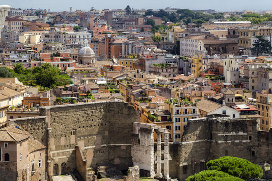 View of the ancient ruins of the Forum of Augustus with surrounding historic buildings, terracotta rooftops, and urban cityscape in Rome, Lazio, Italy.