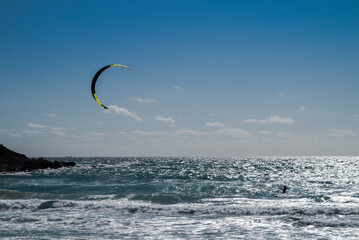 Lone kitesurfer riding the waves off Tarifa, Spain, beneath a large kite silhouetted against a bright sky and sparkling sea, capturing freedom, wind and open space © ihervas