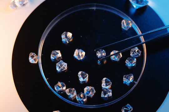 Overhead petri dish filled with laboratory diamonds and tweezers on black plate