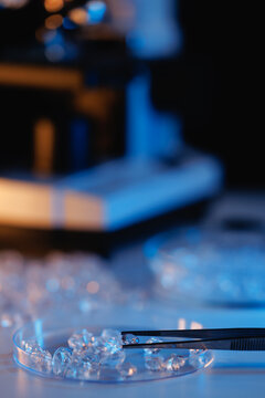 Lab diamonds in petri dish with tweezers and blurred microscope in laboratory setting for jewelry research scientific analysis