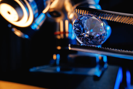 Closeup of single round brilliant cut diamond held by tweezers near microscope for gemology research and jewelry