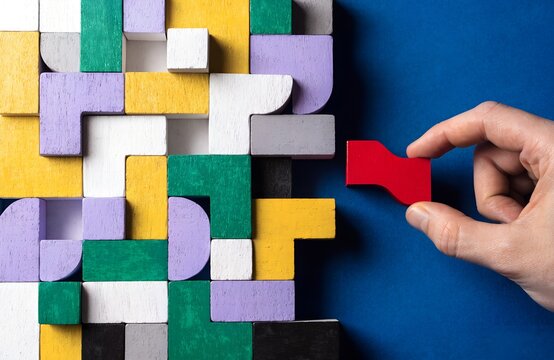 Hand holding red puzzle piece near partially completed colorful wooden block arrangement on bright blue background symbolizing creativity problem solving logical thinking artwork  generated ai