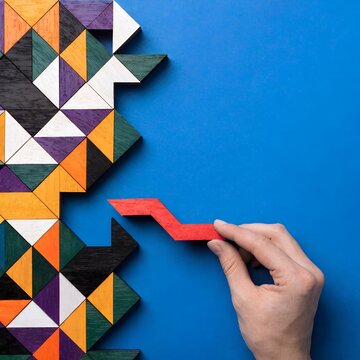 Hand holding red zigzag wooden piece against blue background geometric mosaic of colorful triangles puzzle arrangement symbolizing creativity problem solving logical thinking artwork  generated ai