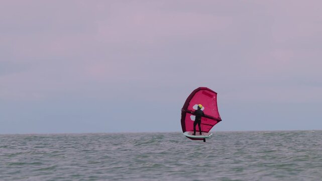 An athlete standing on the board holds on to the wing, in which the wind creates thrust in slow motion. Wingfoil board where a surfer glides through the water on a hydrofoil board.
